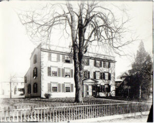 Black and white photo of a three story house with tree in front