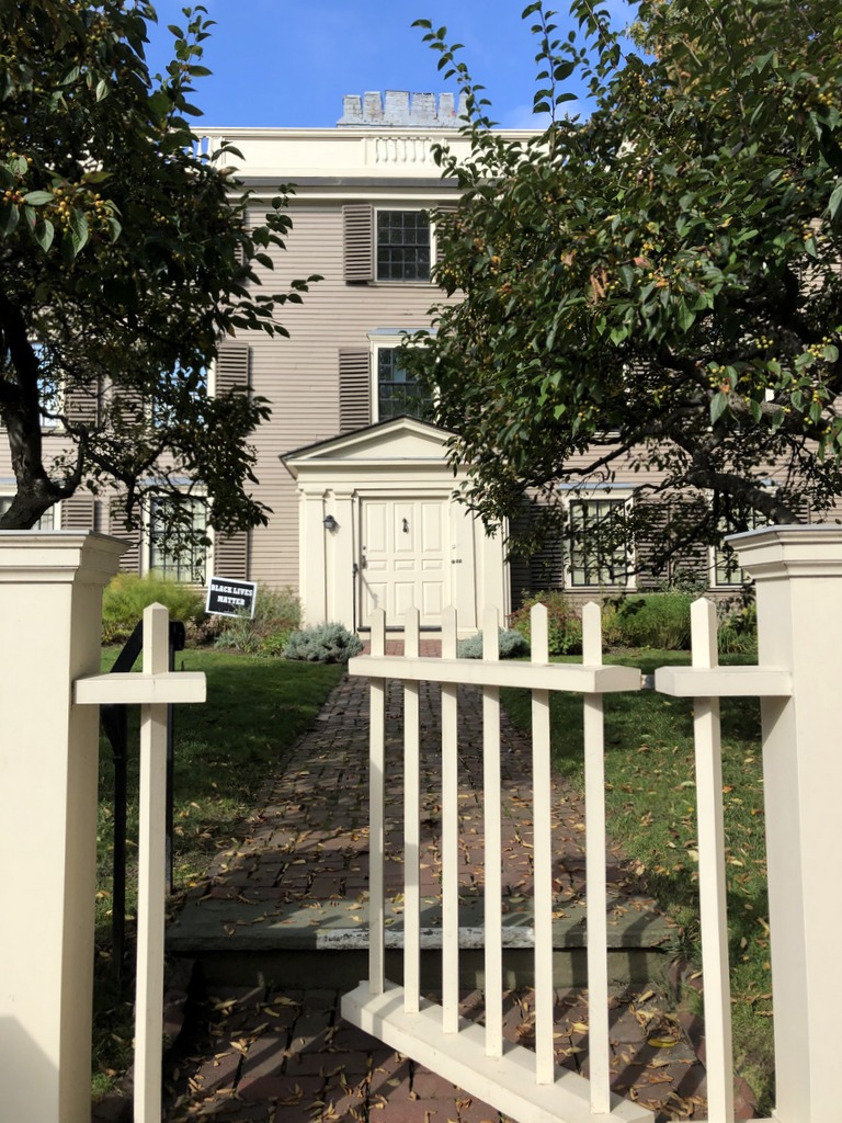 Open front gate leading up to front door of historic house flanked by trees