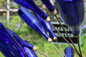 A close up photograph of the bottles on one of the blue bottle trees in the "Forgotten Souls of Tory Row" art installation, with a "Black Lives Matter" sign in the background