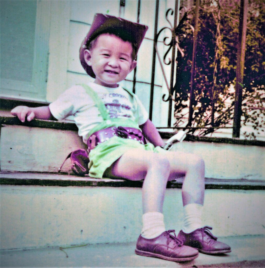 A young boy leaning on the front steps of a house wearing a cowboy hat