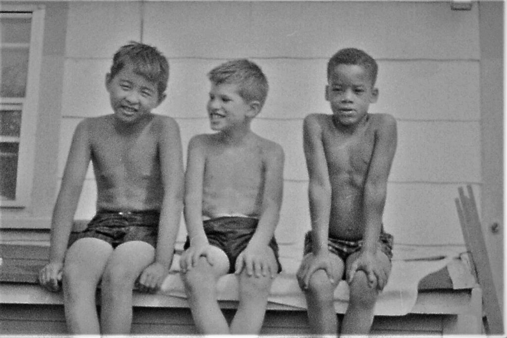 Three boys sitting on a platform wearing shorts.