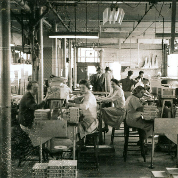 Black and white photo of people seated a tables in a candy factory