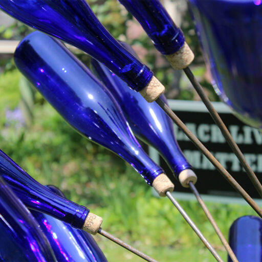 A close up photograph of the bottles on one of the blue bottle trees in the "Forgotten Souls of Tory Row" art installation, with a "Black Lives Matter" sign in the background